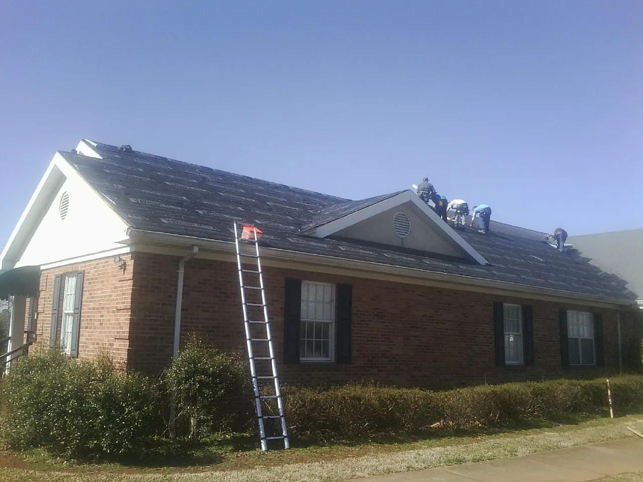 Crew tearing shingles off a brick ranch roof with a ladder set — Metal Roof Repair work by our crew in Mooresville