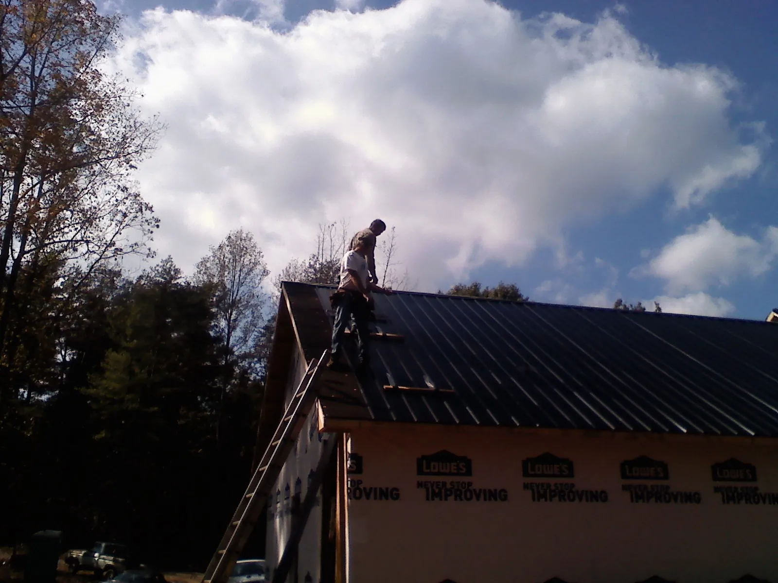 Roofer fastening dark metal panels high against a cloudy sky, from a Roof Inspection job in Mooresville