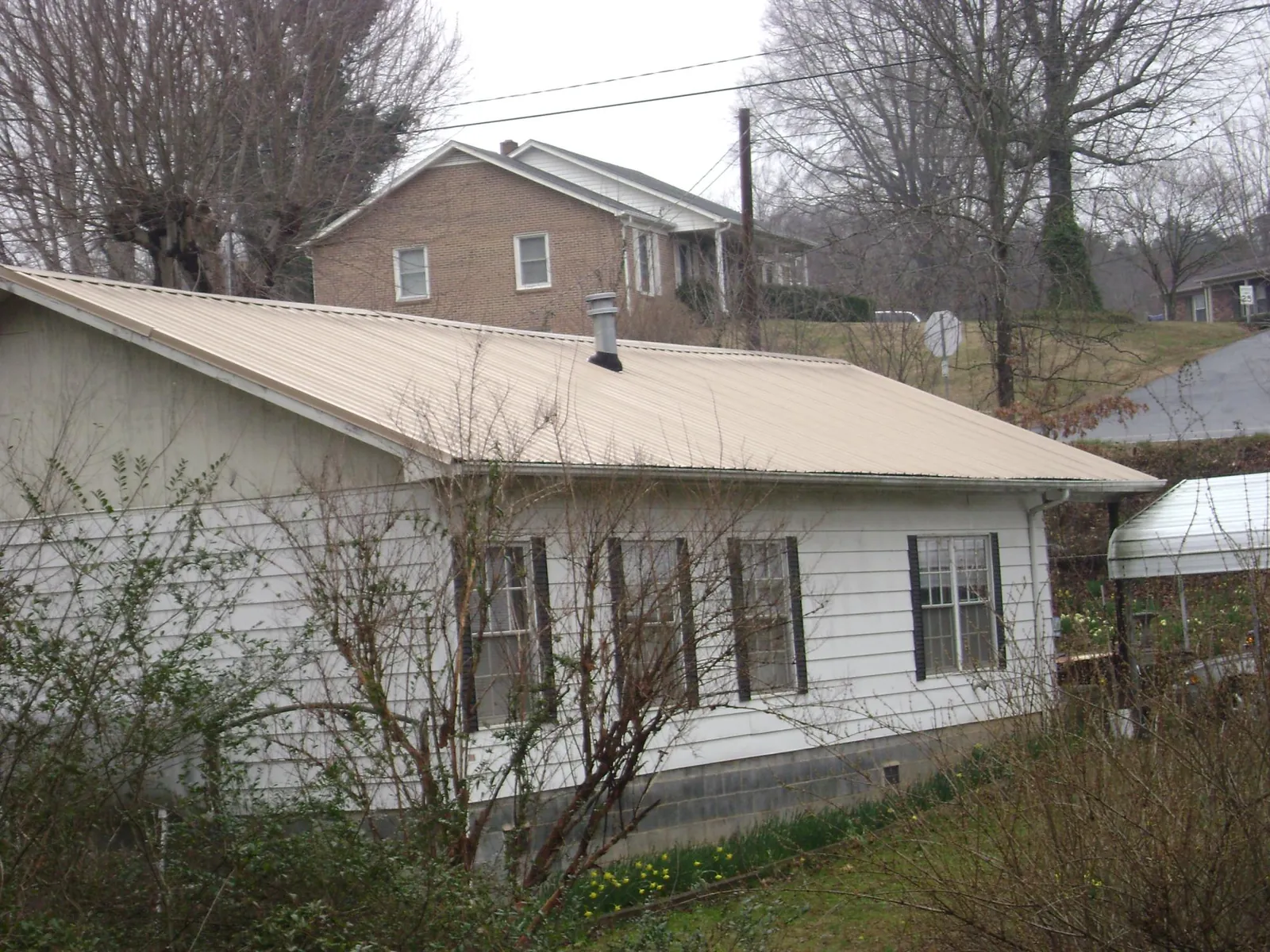 Tan metal roof on a white sided house set into a hillside — Commercial Roofing by Roofing Brothers in Mooresville